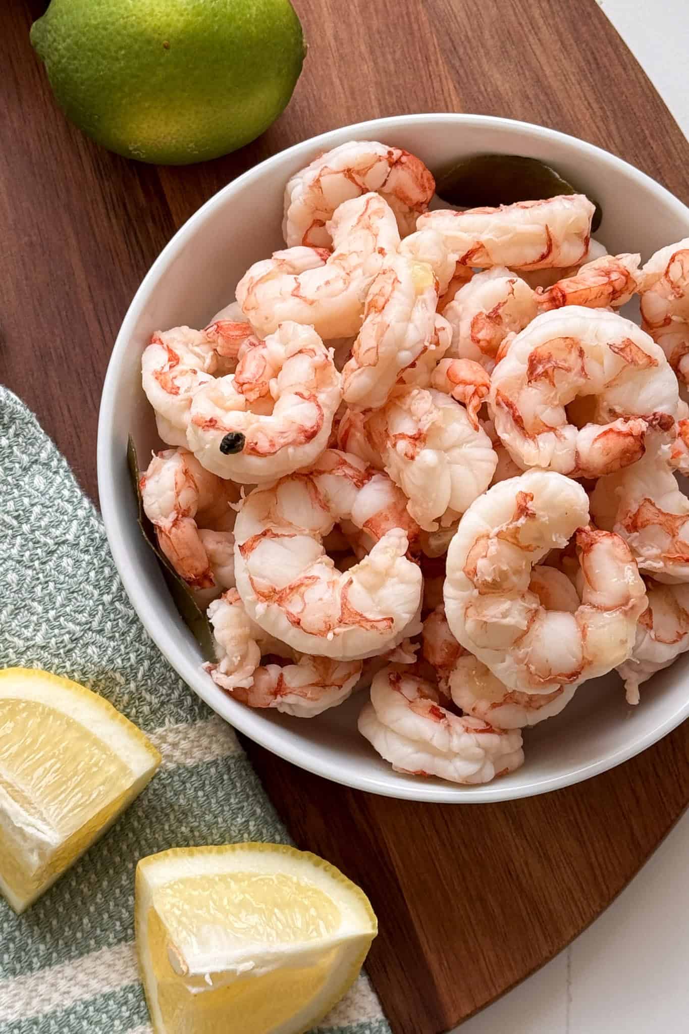 Bowl of boilded shrimp with limes and lemon wedges on a wooden board