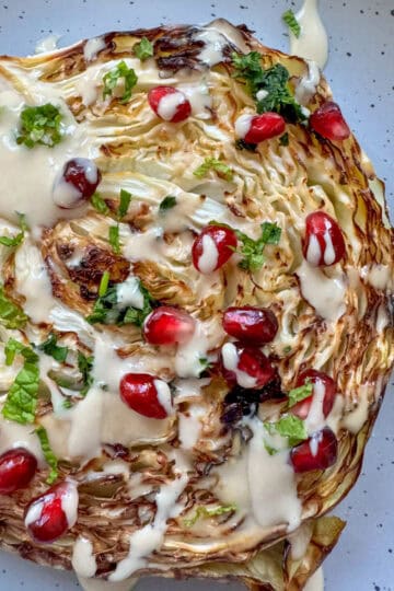 roasted cabbage on a plate drizzled with tahini and pomegranate seeds